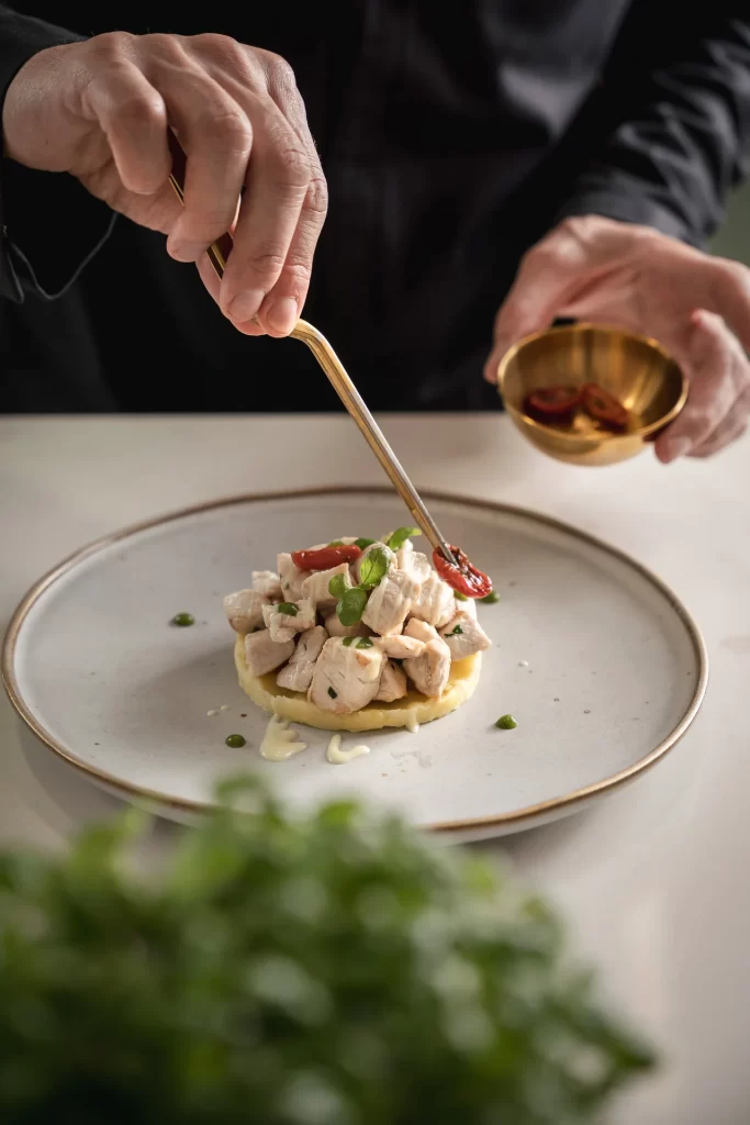 Chef che guarnisce un piatto elegante di pollo con verdure su un piatto bianco.