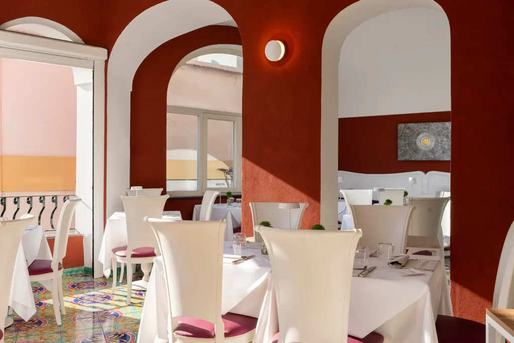 Interno di un elegante ristorante con pareti rosse, sedie bianche e pavimento colorato.