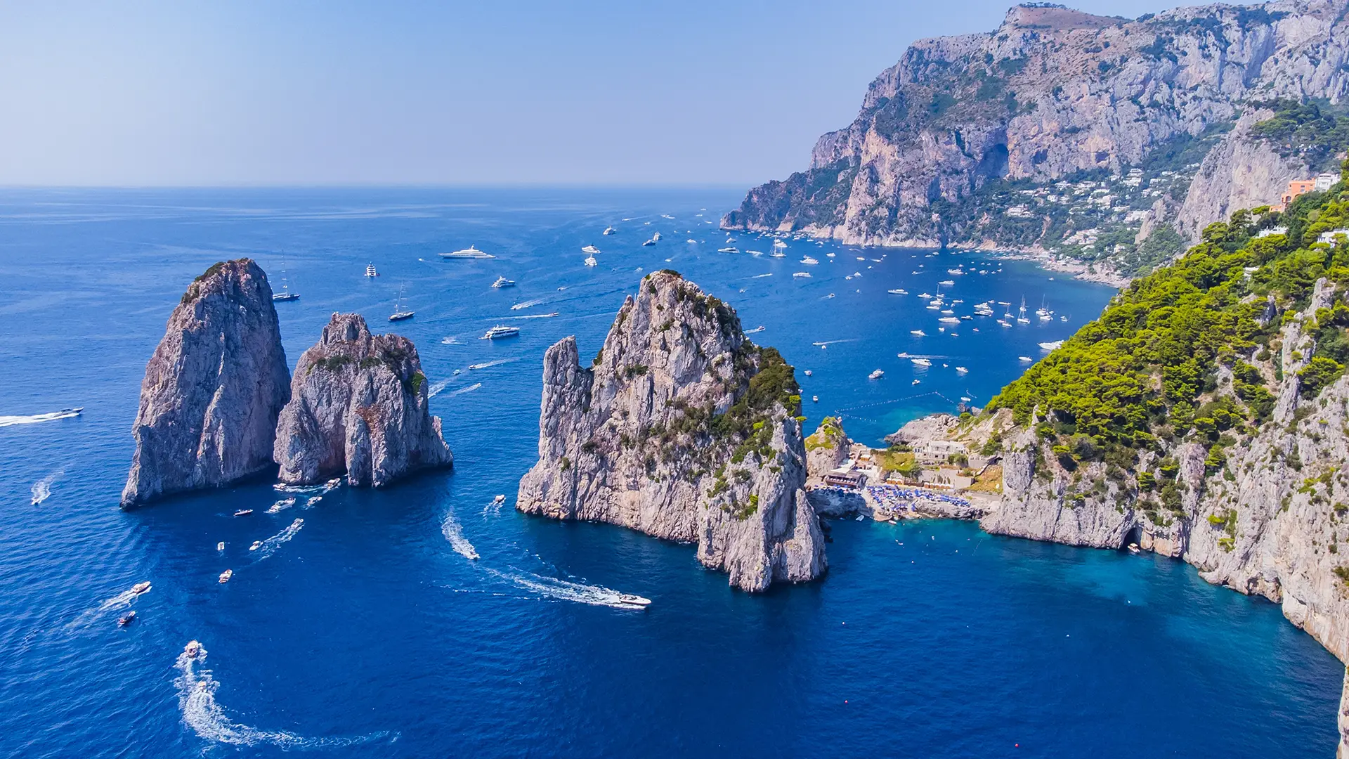 A stunning aerial view of rocky cliffs and boats on the vibrant blue sea near a coastal island.