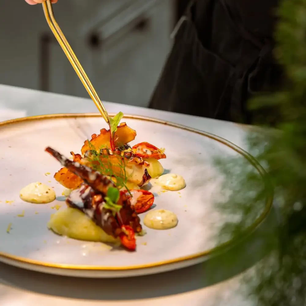 Chef che impiatta un sofisticato piatto di gamberi con decorazioni gourmet.