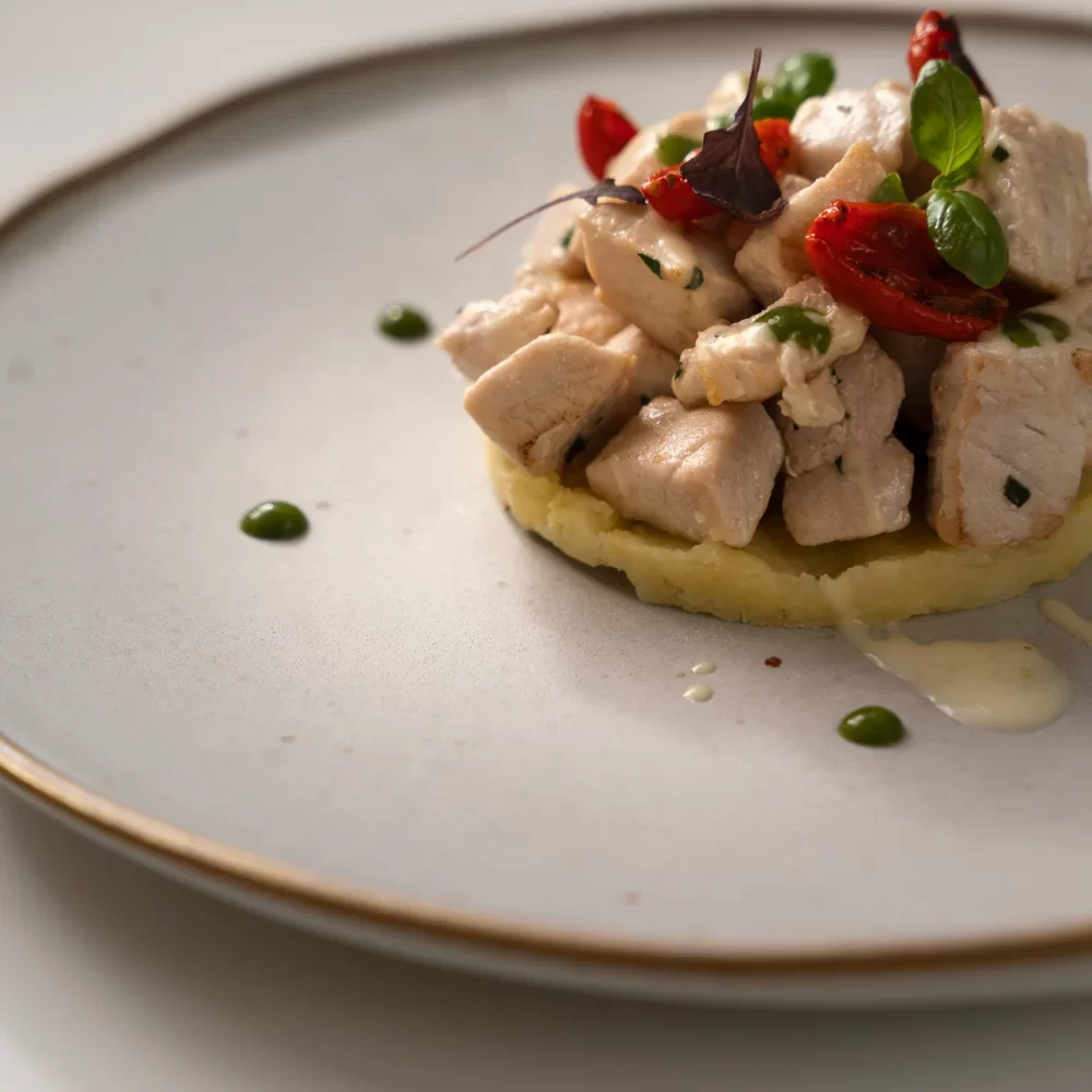 Piatto gourmet con pezzetti di pollo su base di purè di patate decorato con erbe e pomodorini.